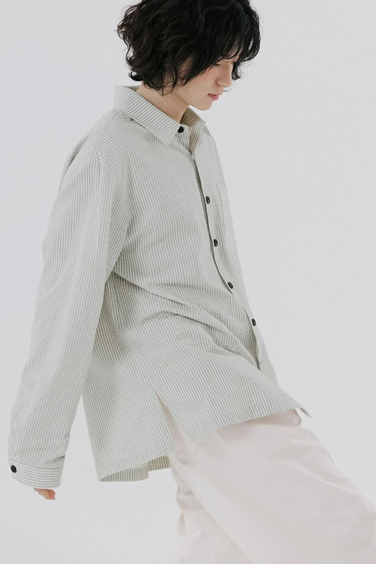 Person wearing a light beige striped button-up shirt with black buttons and cream pants on white background