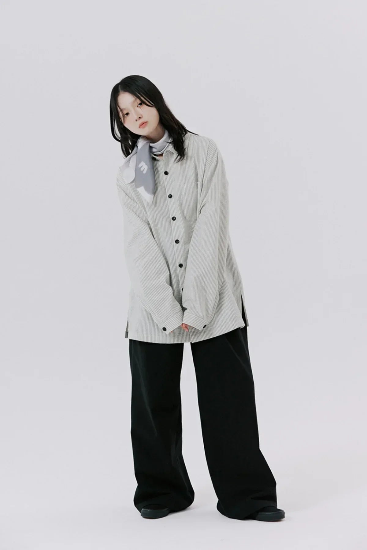Model wearing oversized light striped button-up shirt, black wide-leg pants, and gray scarf on plain background