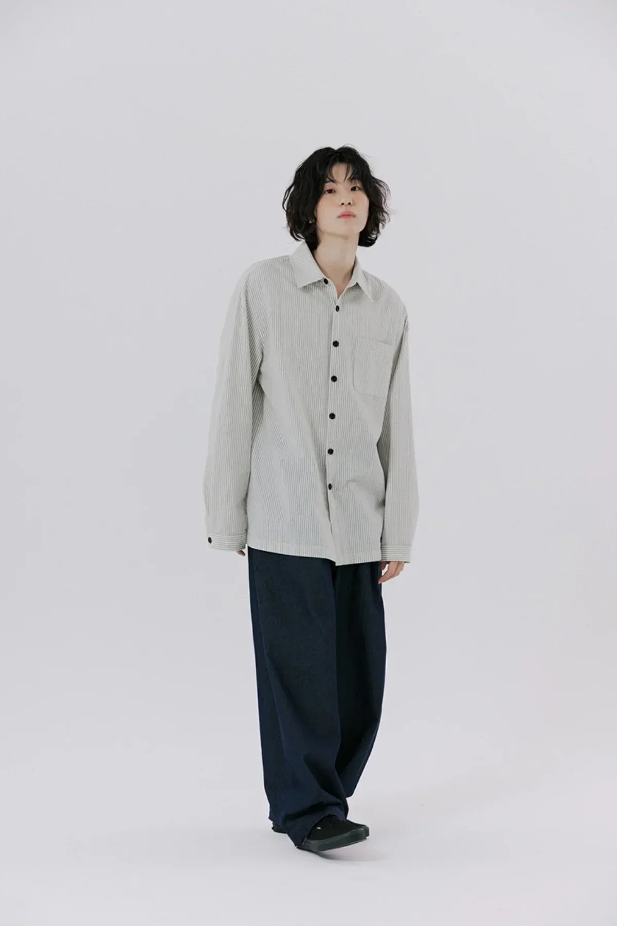 Model in striped oversized button-up shirt and loose dark pants on plain white background