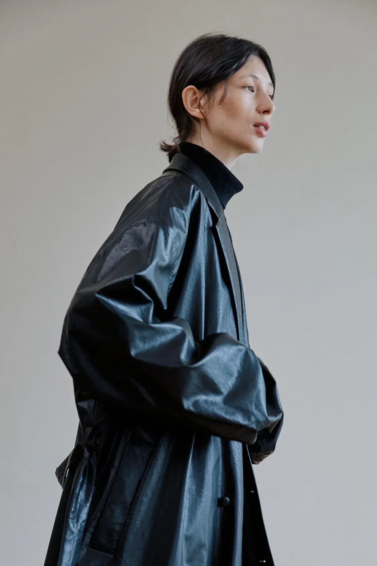 Close-up side view of person wearing black unisex leather trench coat over black turtleneck