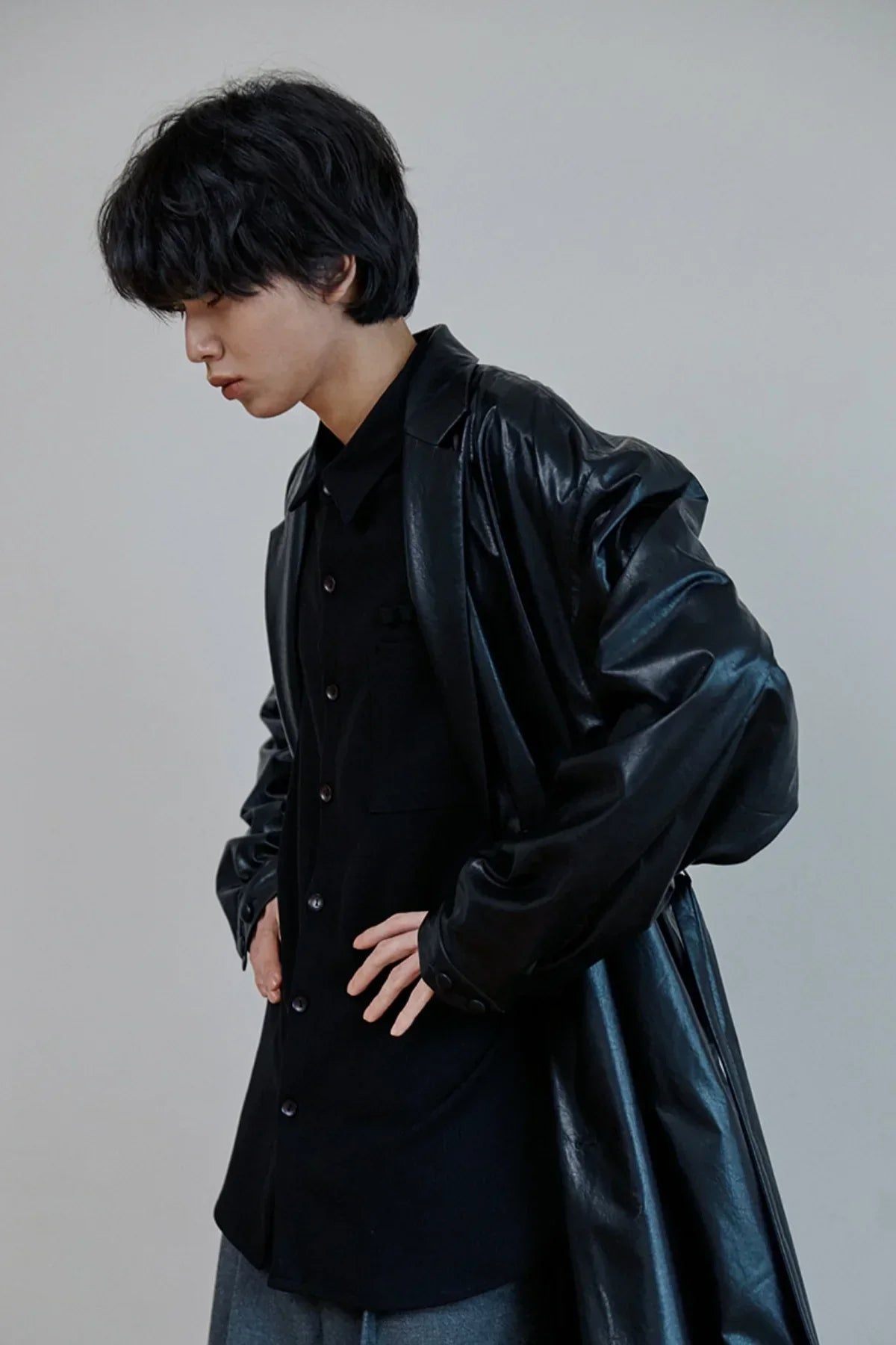 Side profile of a person wearing a black leather trench coat over a black shirt against gray background
