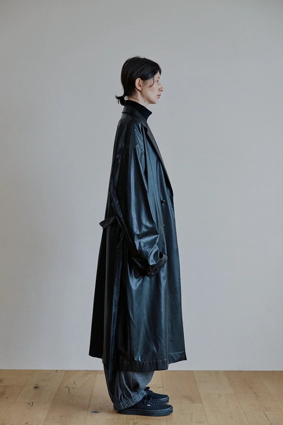 Side view of person wearing long black unisex leather trench coat with black turtleneck and pants