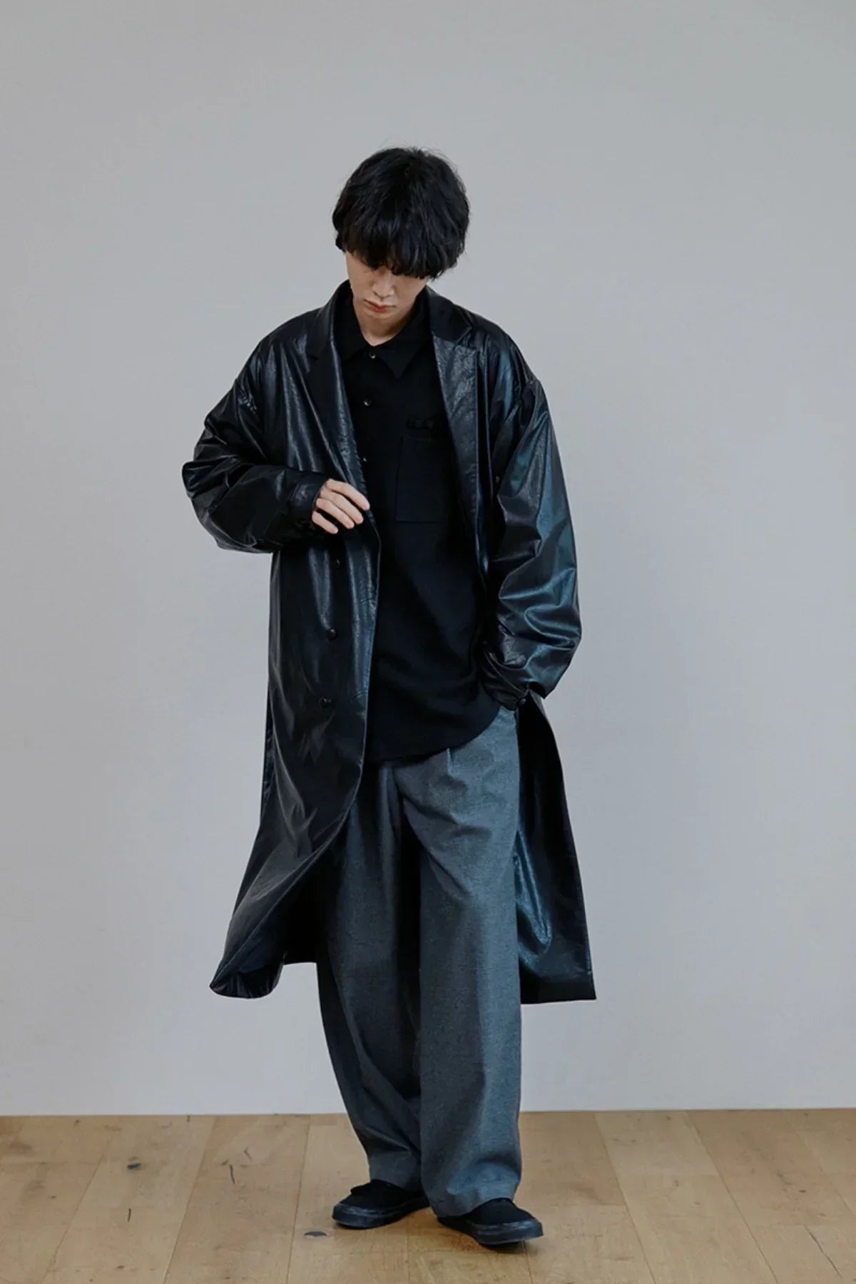 Model wearing long black leather trench coat with loose gray pants and black shirt in studio
