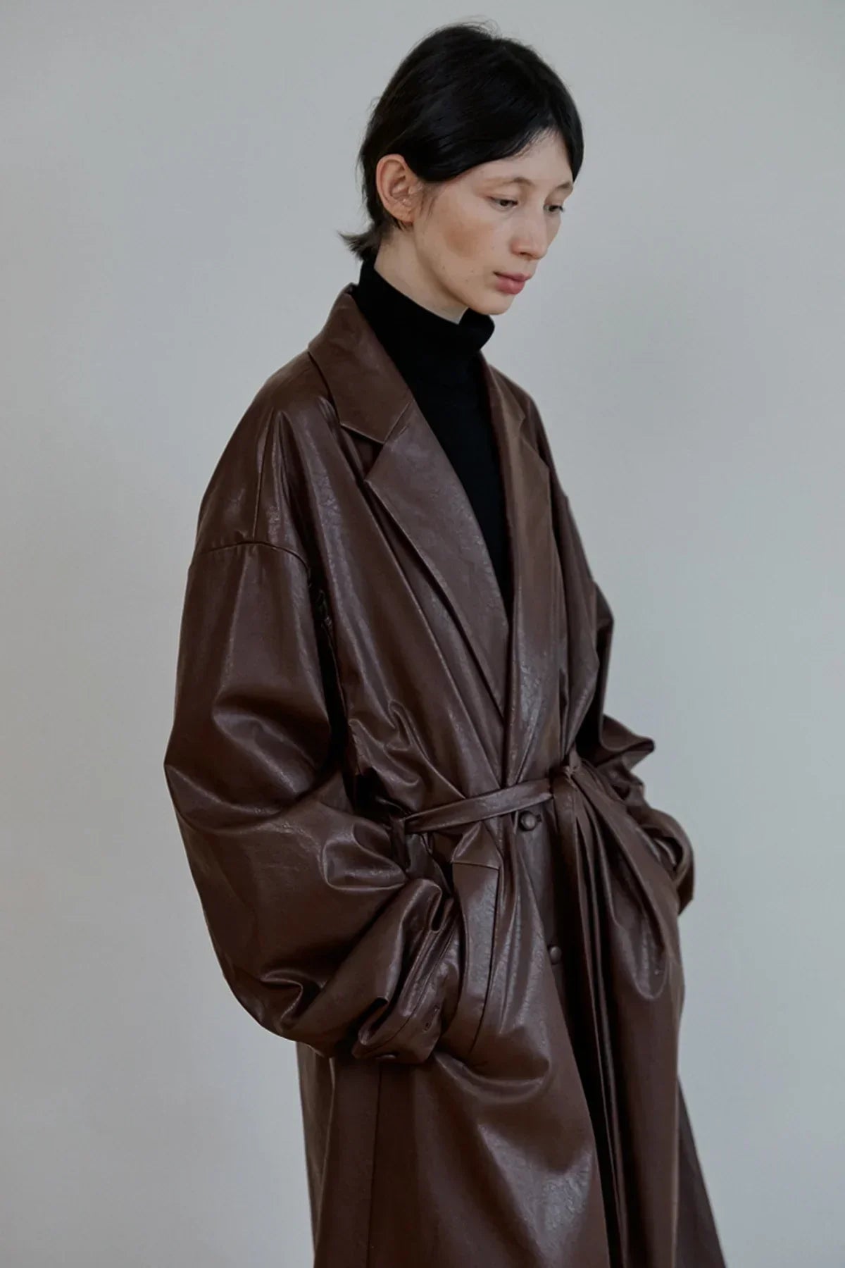 model wearing a brown oversized leather trench coat with a belt over a black turtleneck