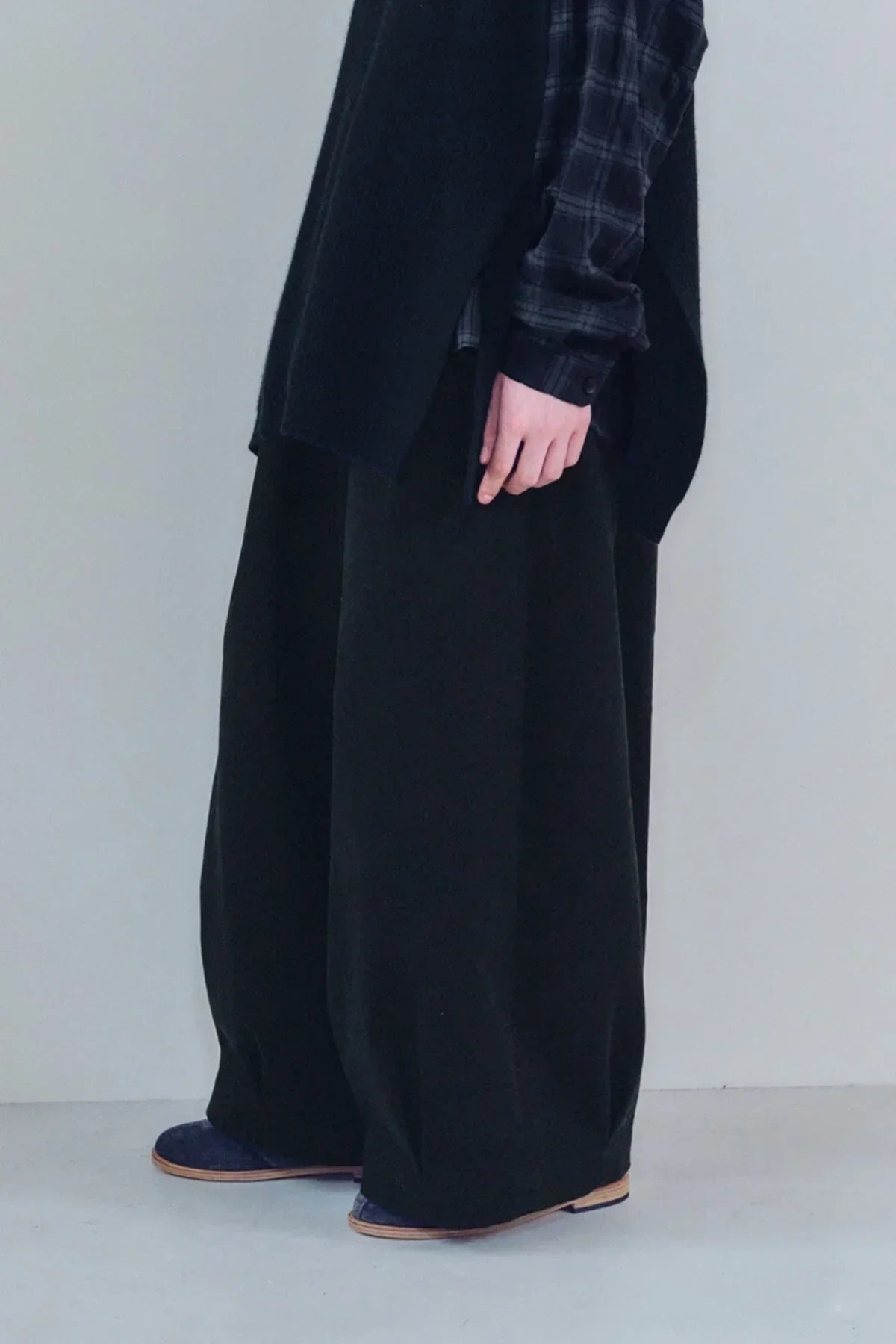 Close-up of unisex black tuck balloon pants worn with black plaid shirt and dark shoes
