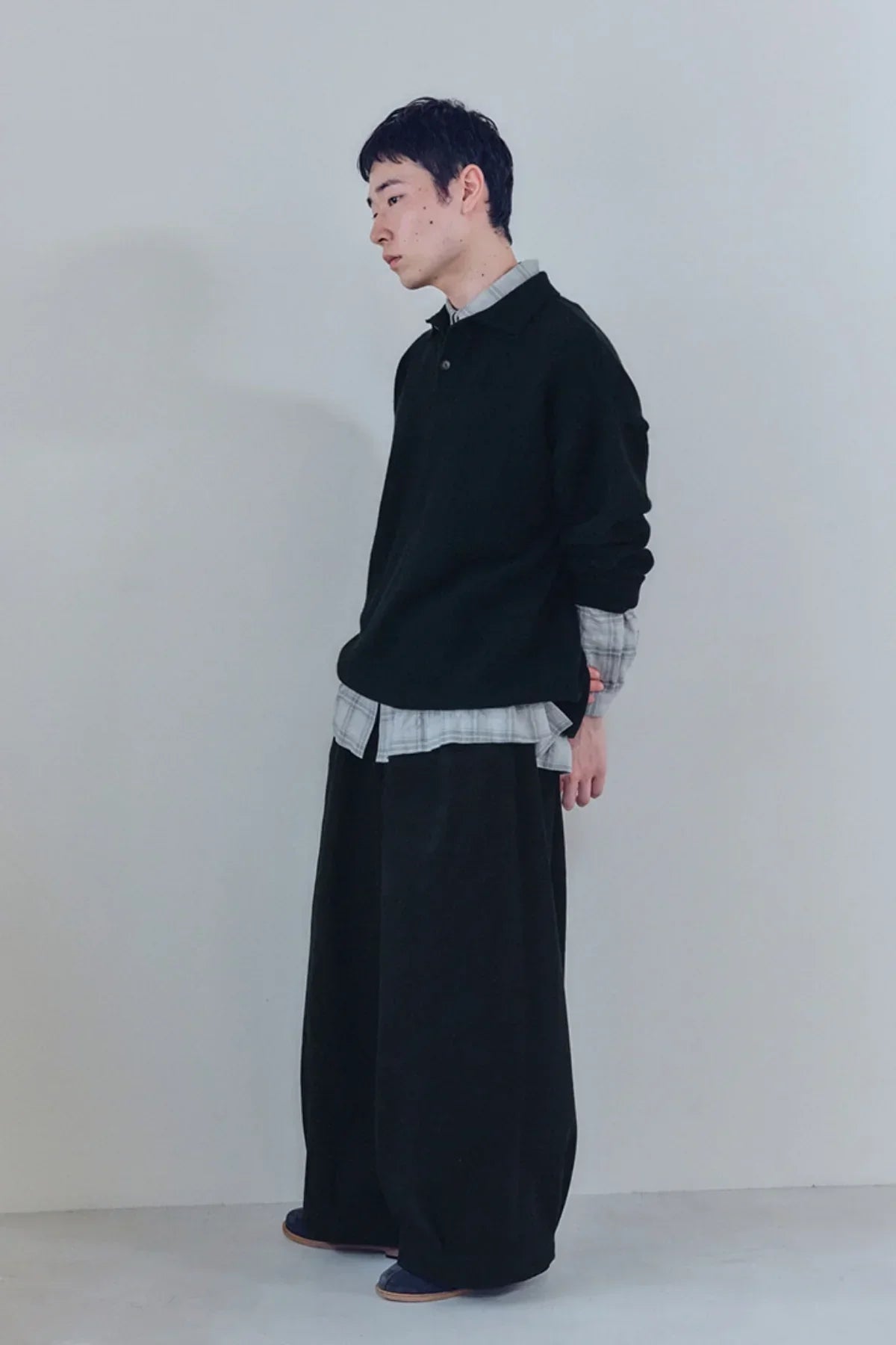 male model wearing black unisex tuck balloon pants with black top and plaid shirt