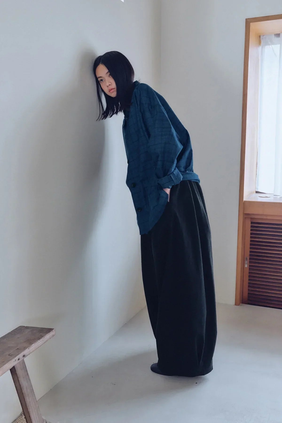 Woman wearing unisex black tuck balloon pants and blue plaid oversized shirt in minimal room