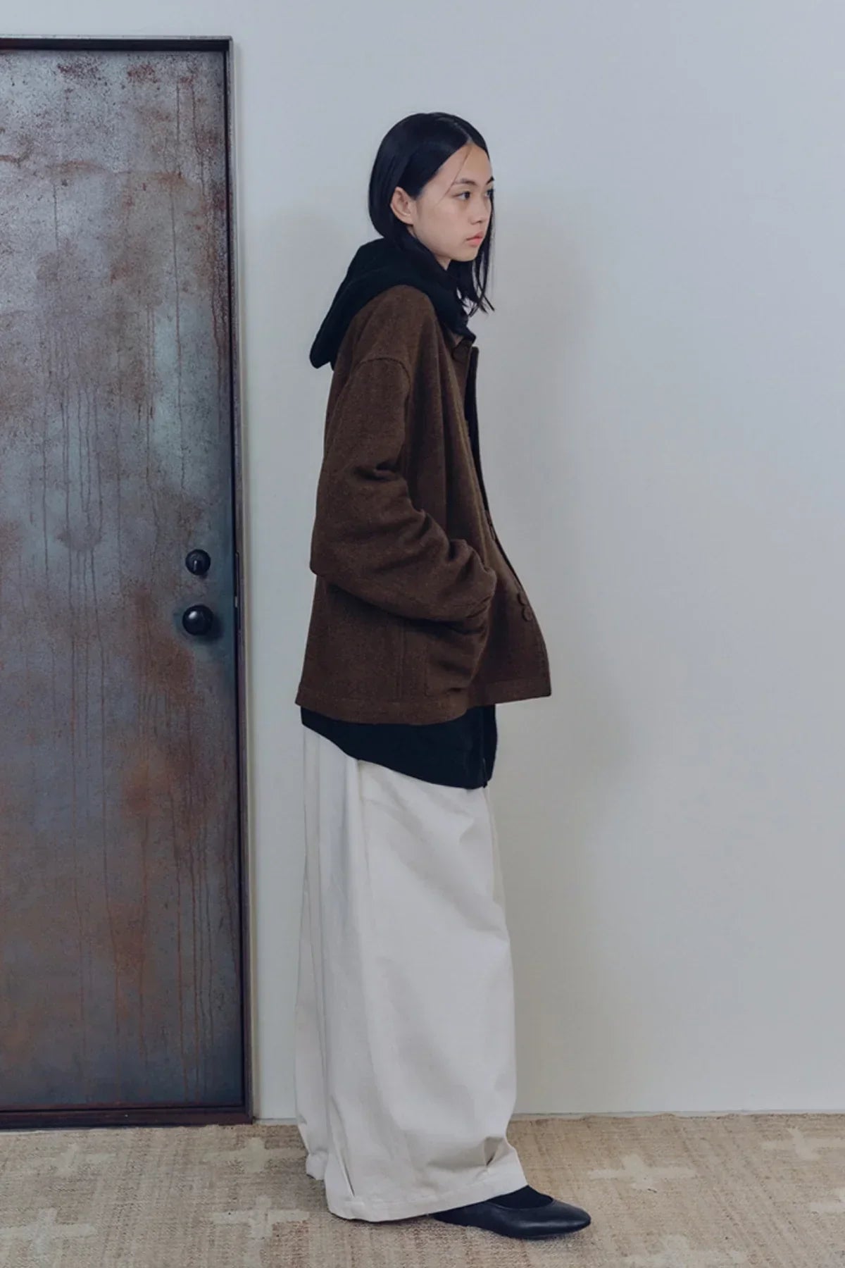 Model wearing unisex cream tuck balloon pants with brown jacket and black shoes indoors