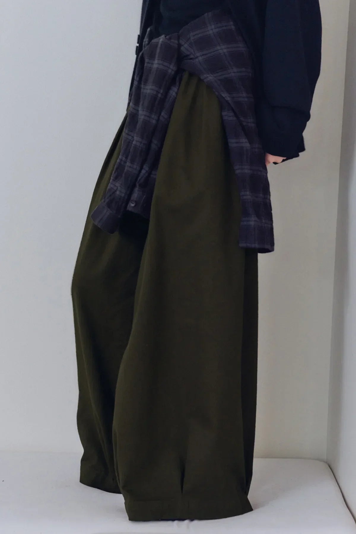 Close-up of unisex khaki tuck balloon pants styled with a tied plaid shirt