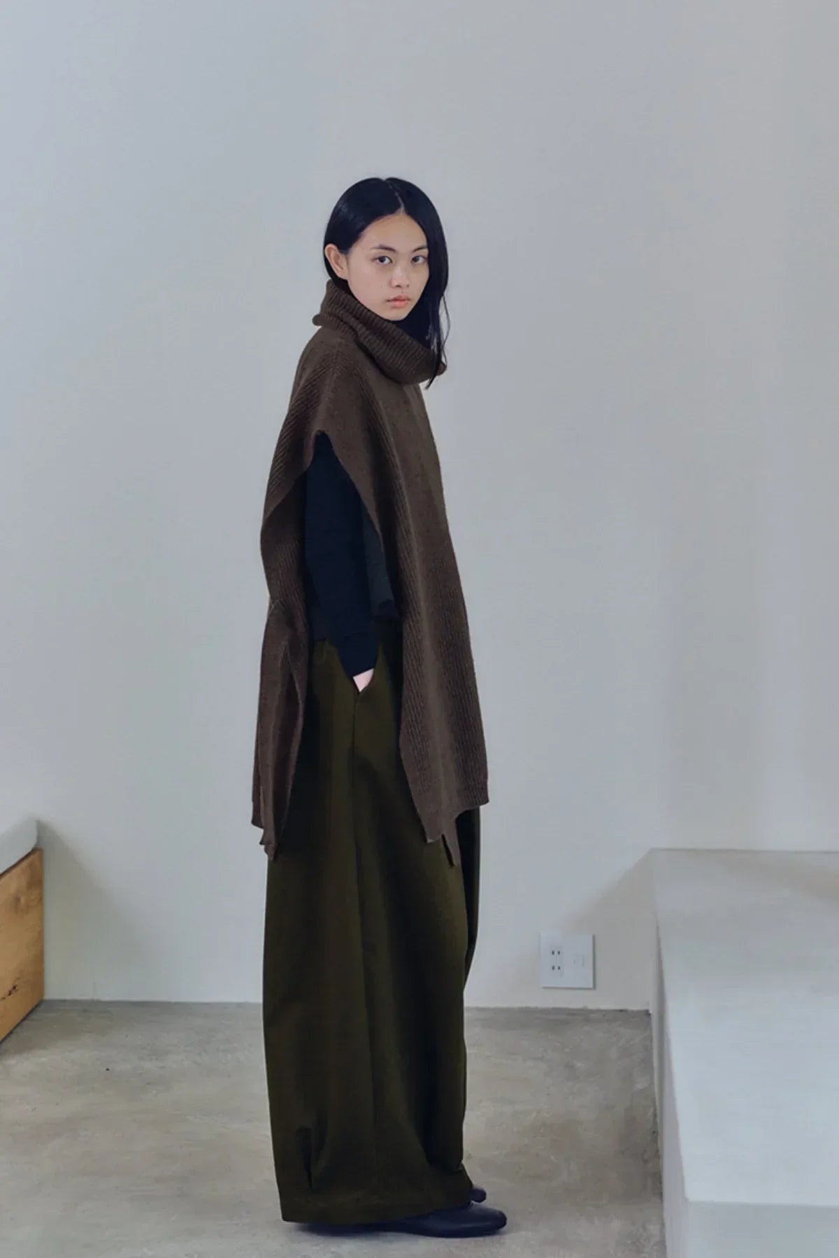 Side view of woman wearing loose khaki balloon pants and a brown knitted sleeveless turtleneck