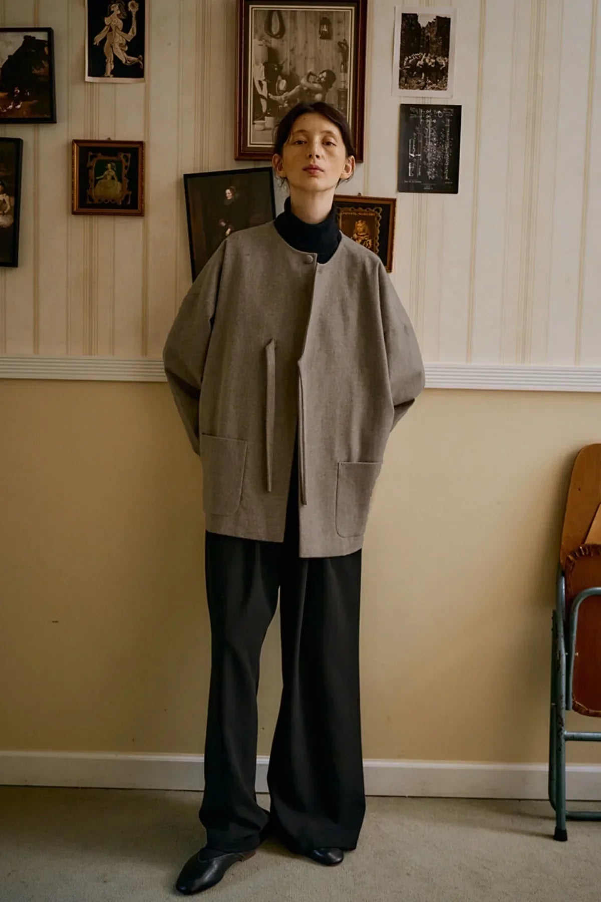 Model wearing oversized beige wool jacket with pockets, black wide pants, and black shoes in vintage room