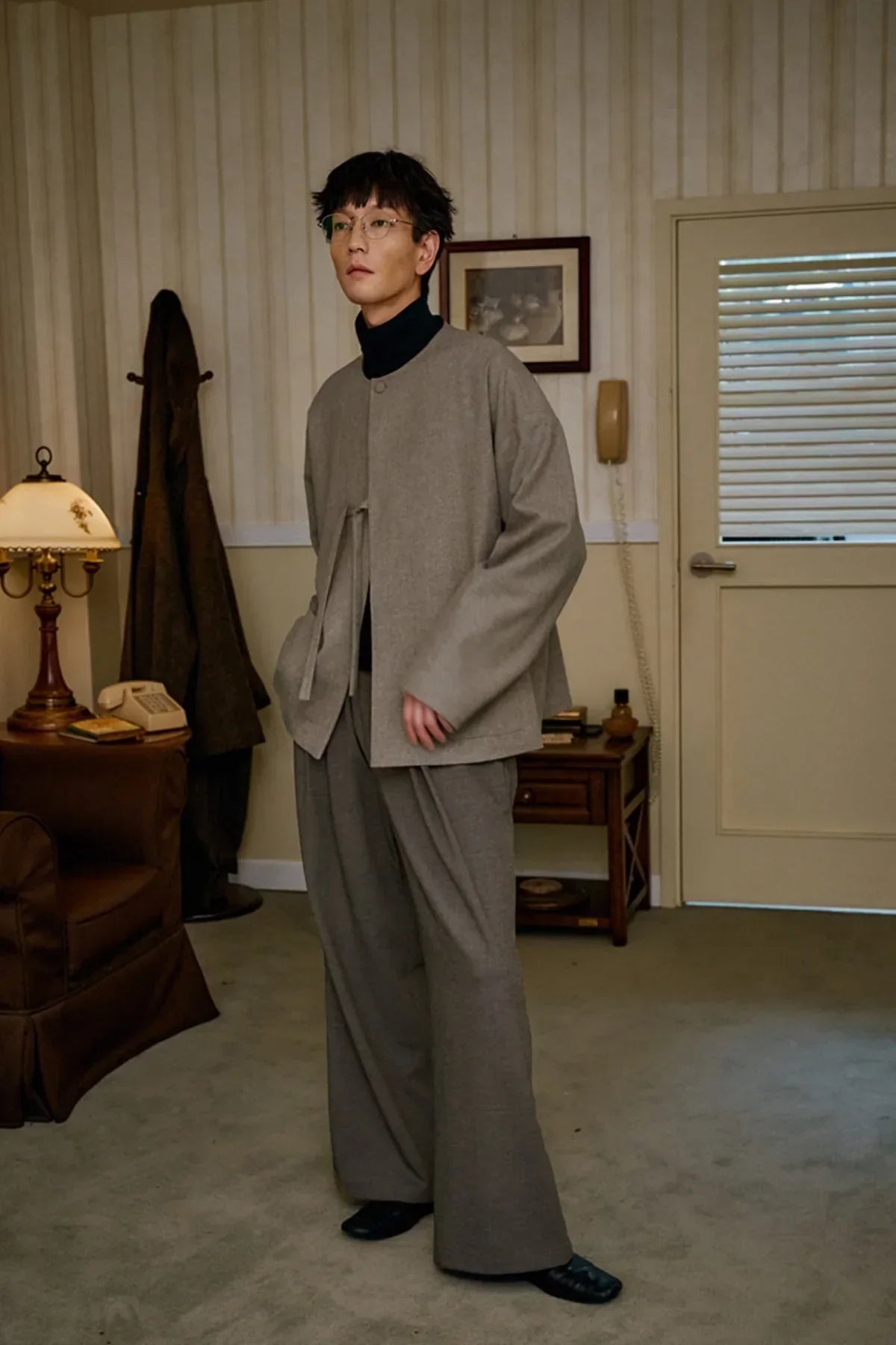 Asian man wearing beige wool loop jacket and wide gray pants in vintage styled living room