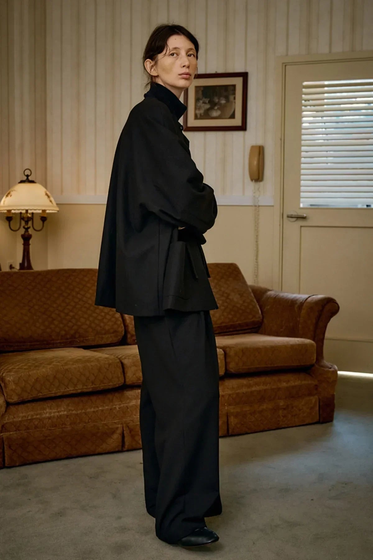 model wearing unisex black wool loop jacket and wide pants standing in vintage living room