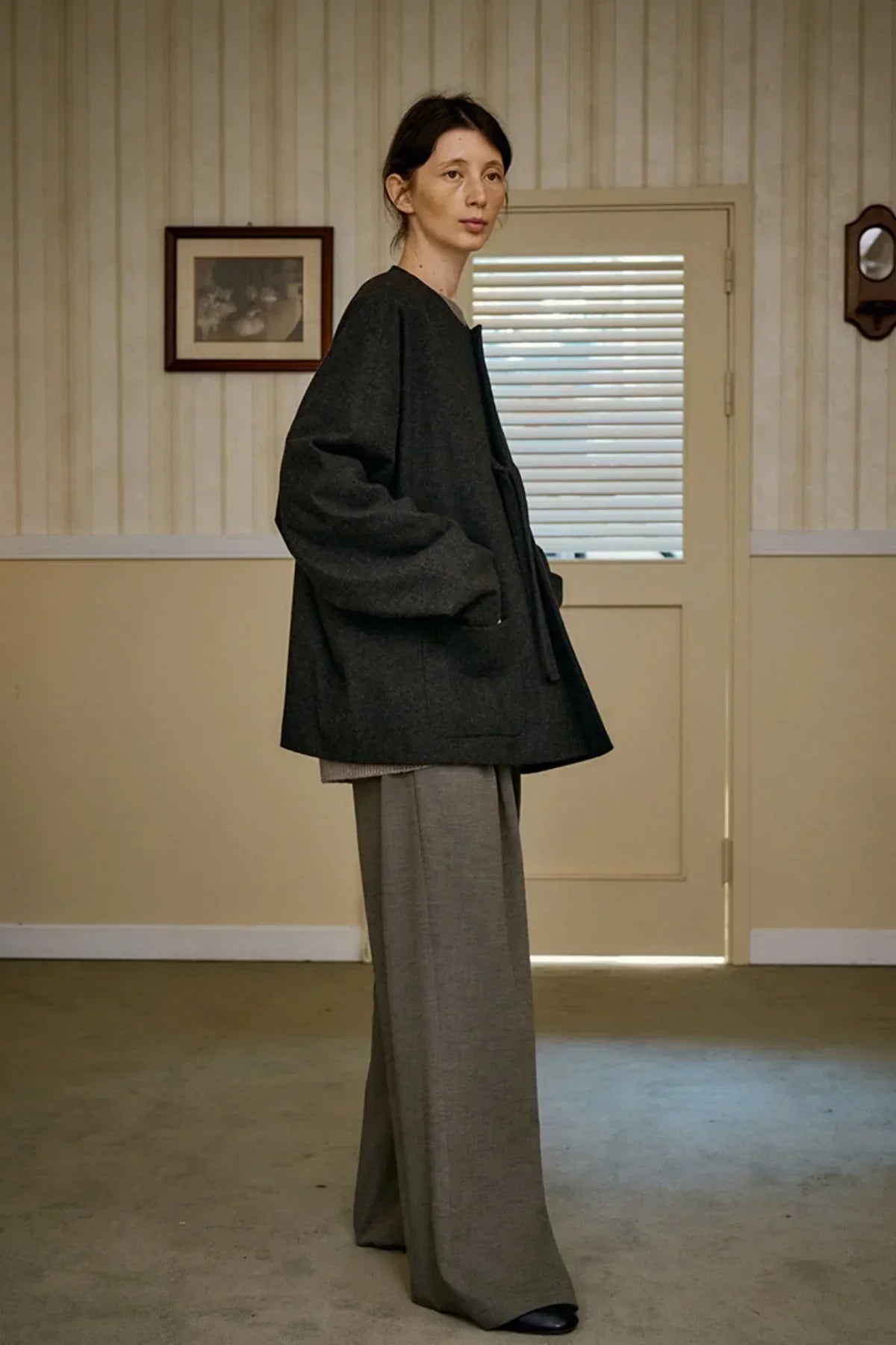 Model wearing charcoal unisex wool loop jacket with wide gray pants in a minimalist room