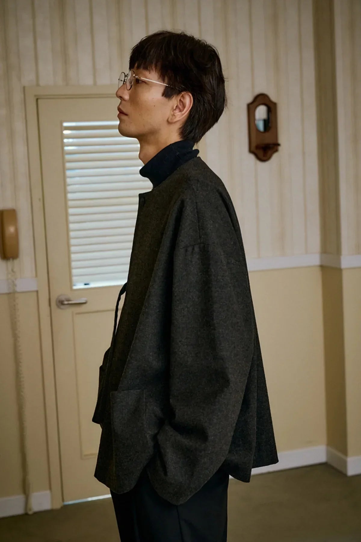 Side view of a man wearing a charcoal wool loop jacket and glasses indoors