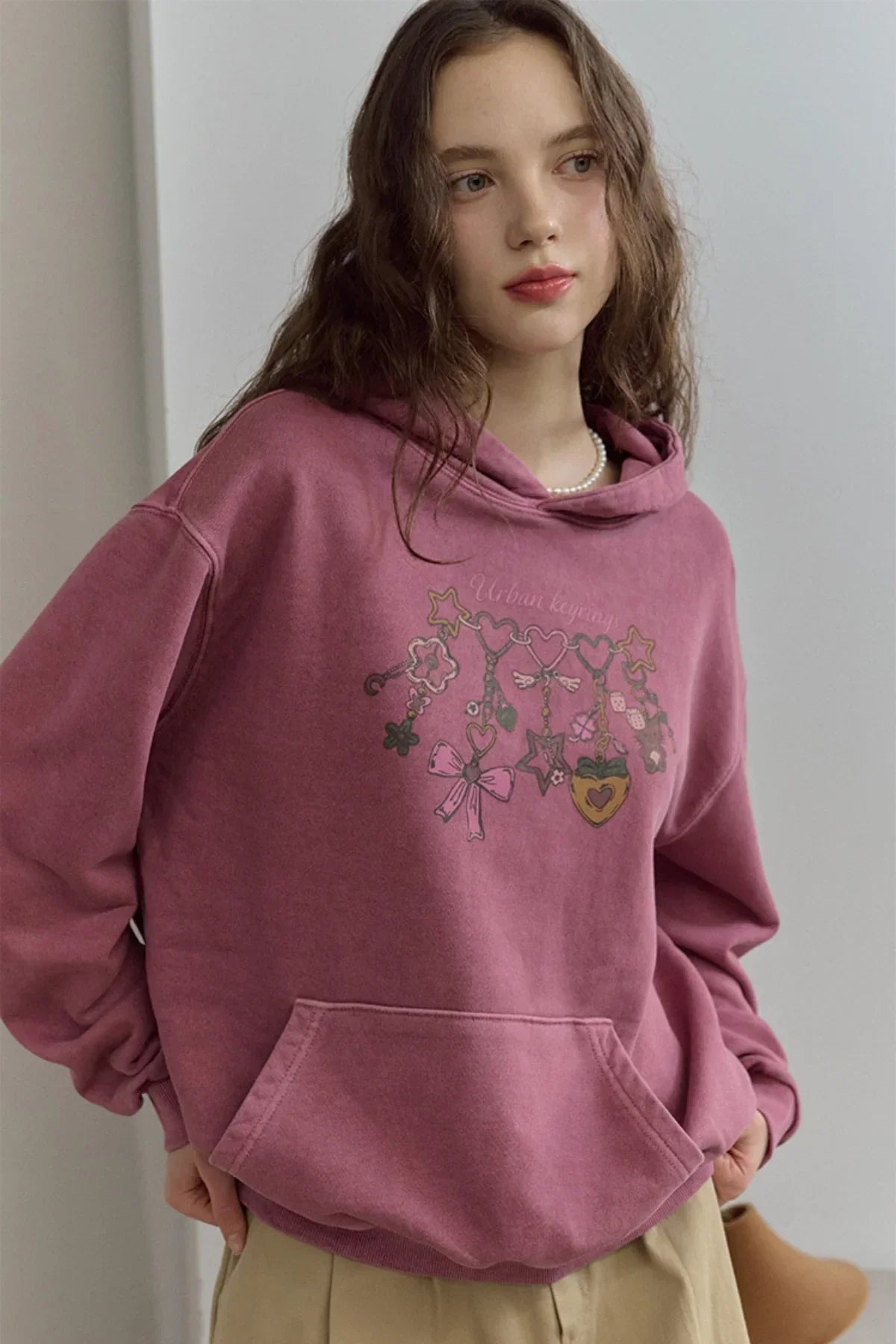 Woman wearing dusty pink hoodie with 'Urban keyring' graphic and beige pants indoors
