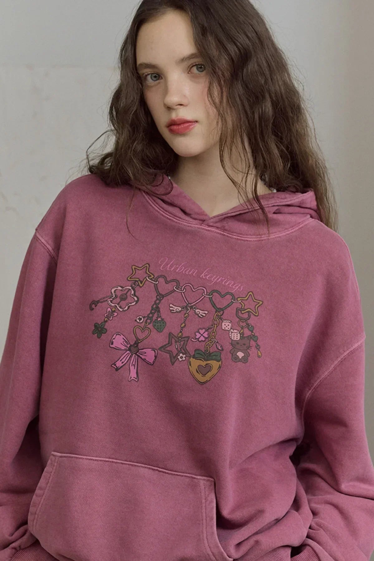 Young woman wearing dusty pink hoodie with colorful urban keyrings graphic print close-up