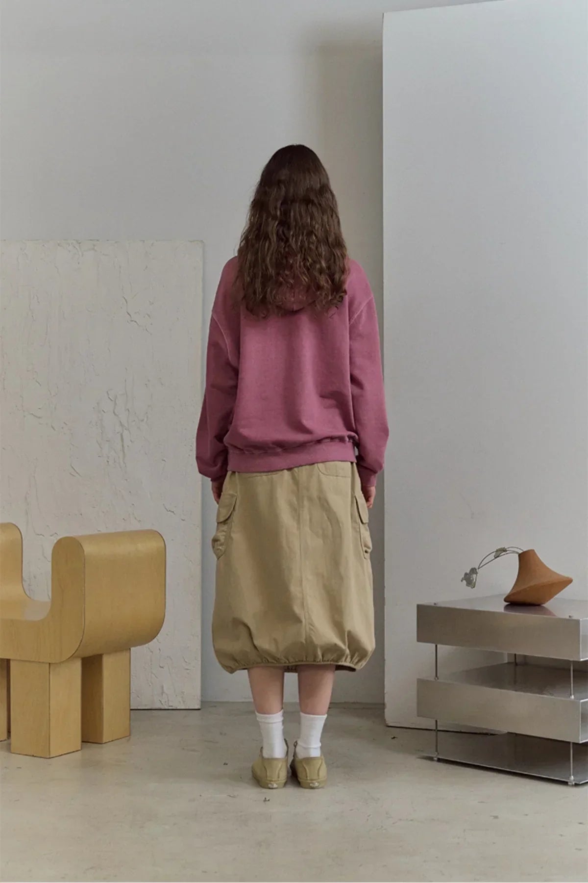 Back view of person wearing dusty pink pigment hoodie and beige bubble skirt in minimalist room