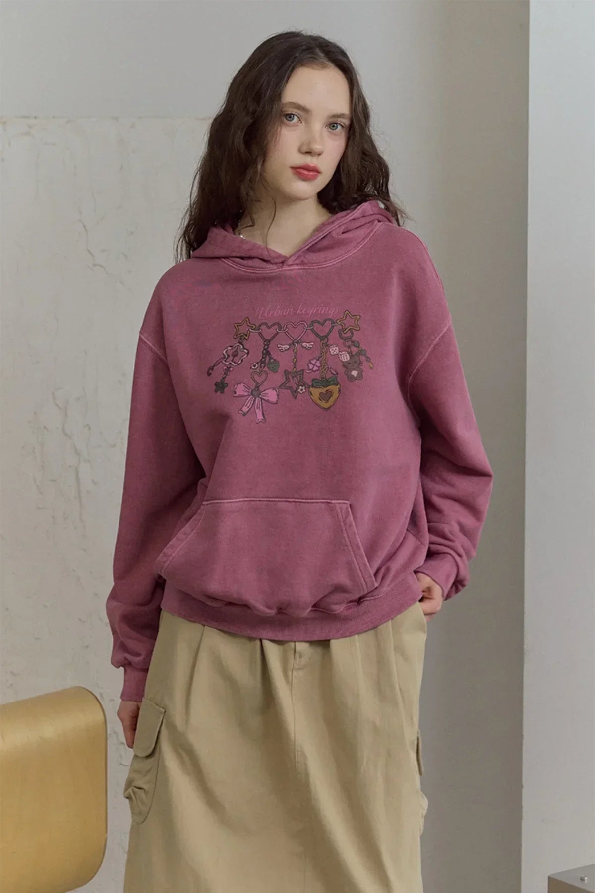 woman wearing dusty pink pigment hoodie with urban keyrings print and beige cargo skirt indoors
