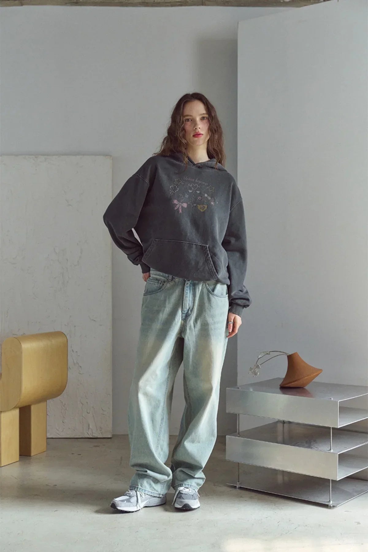 Woman wearing smoke black pigment hoodie and loose light wash jeans in minimal modern room