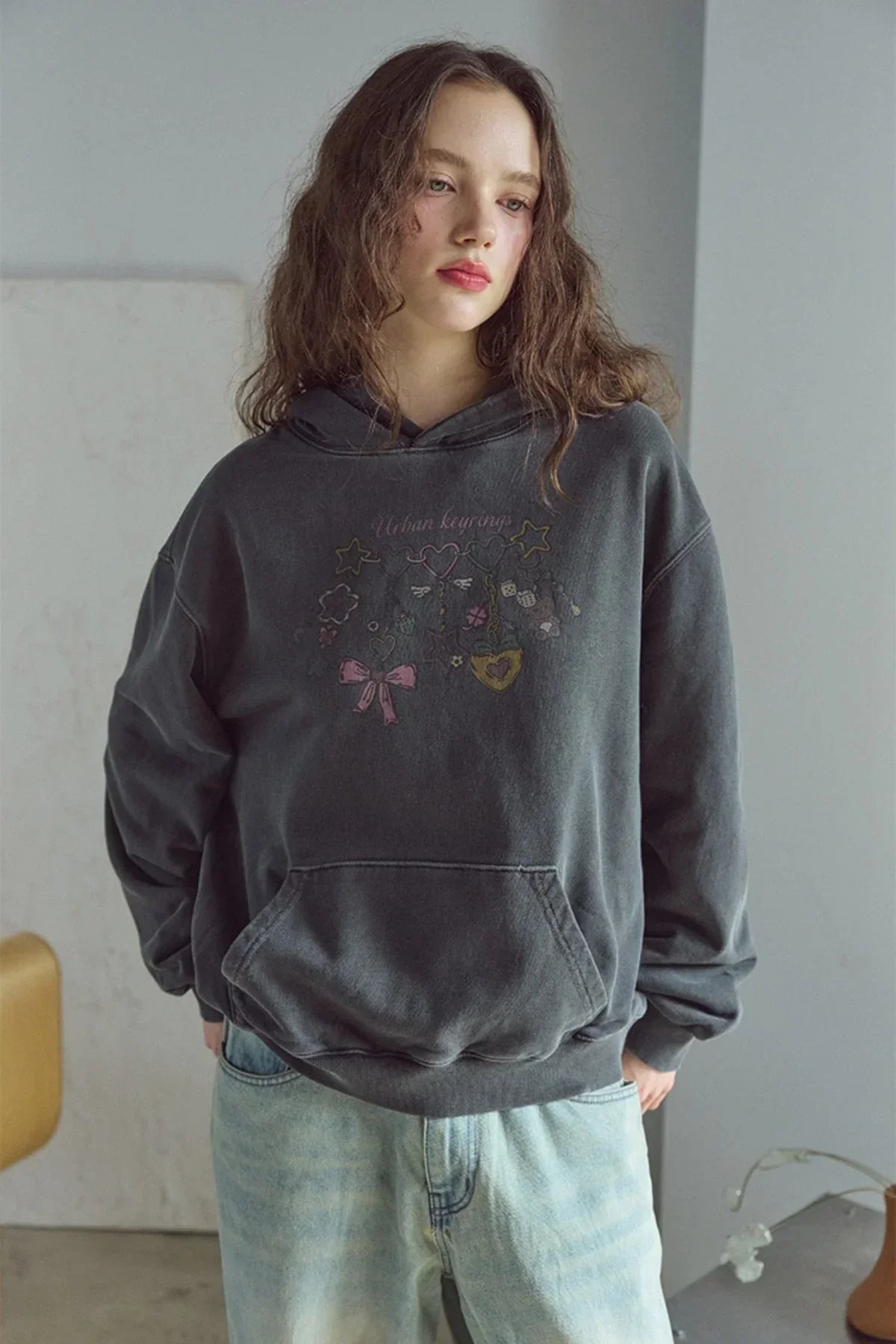 Young woman wearing smoke black pigment hoodie with urban keyrings graphic and light washed jeans indoors
