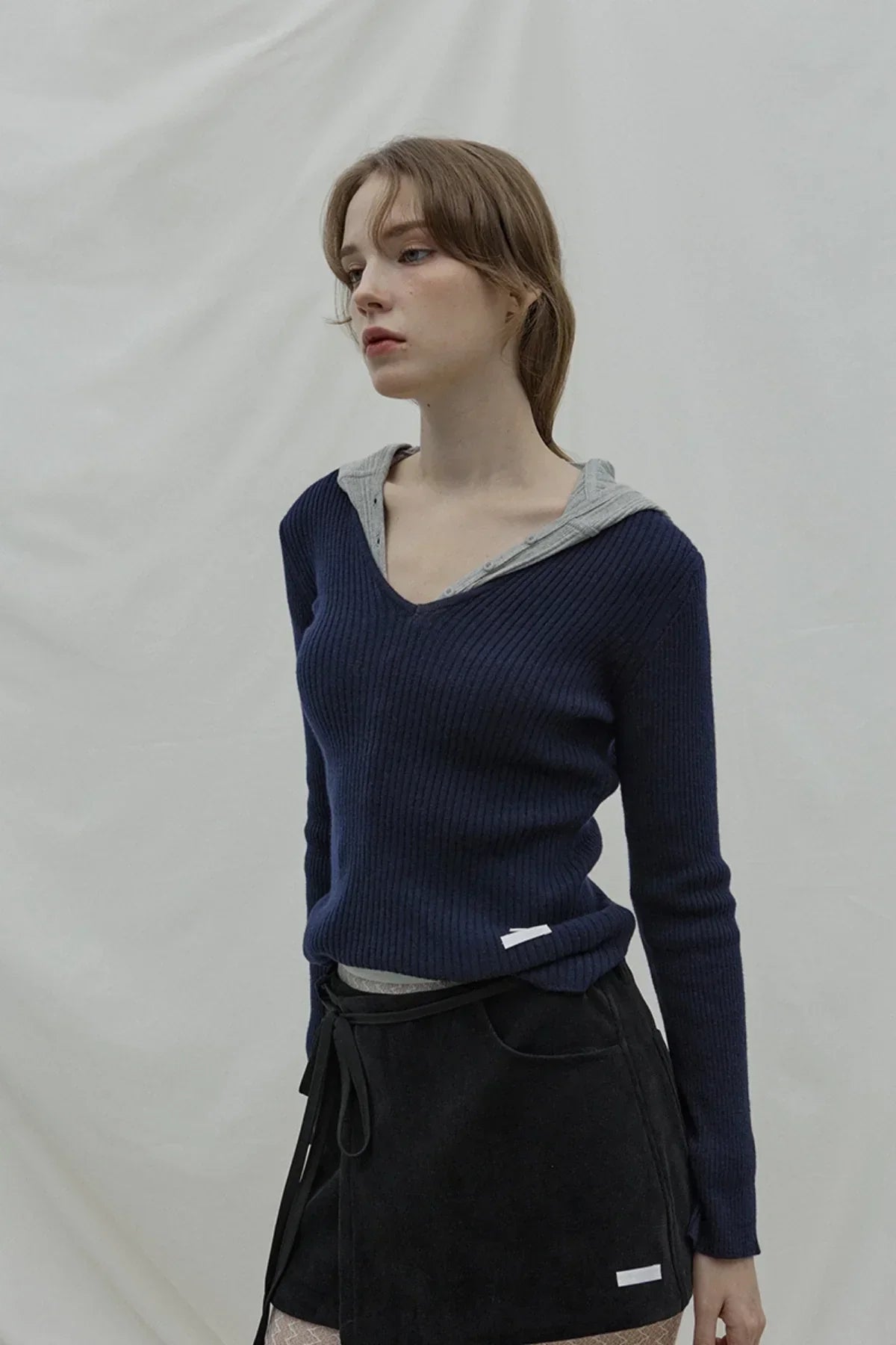 Woman wearing navy blue ribbed v-neck cashmere sweater with gray hood and black wrap skirt