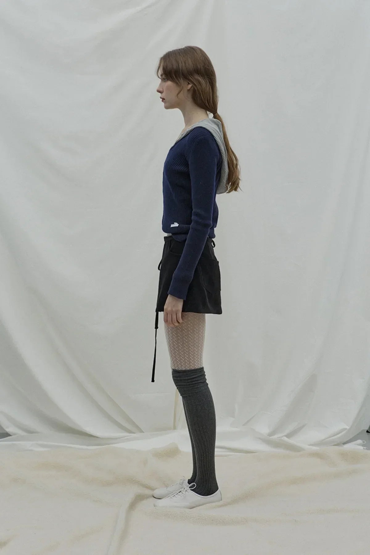 Side view of woman in navy V-neck cashmere sweater, black shorts, patterned tights, and grey knee-high socks