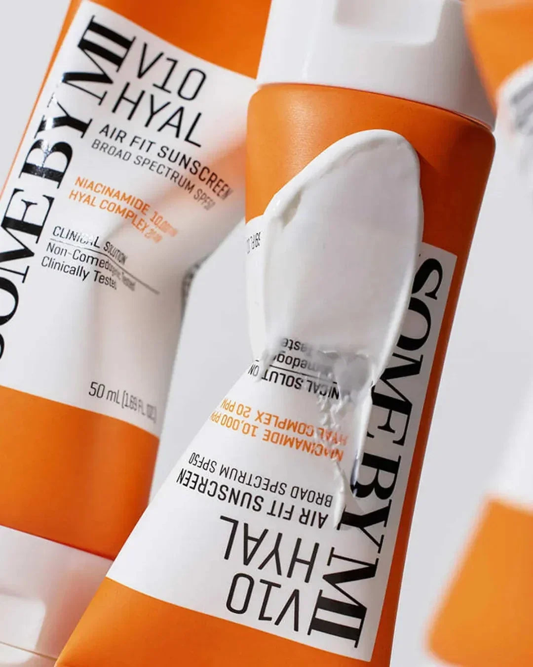 Close-up of orange and white V10 Hyal Air Fit Sunscreen tubes with cream applied, broad spectrum SPF product