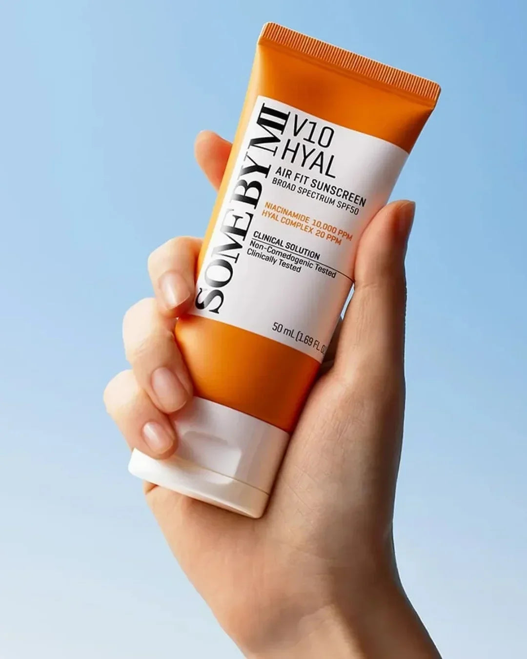 Hand holding SOMEBYMI V10 Hyal Air Fit Sunscreen SPF50 tube against blue background