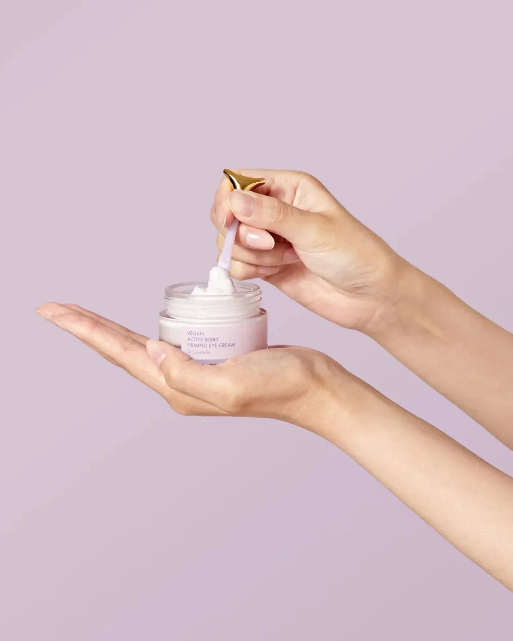 Hands holding vegan active berry firming eye cream jar and scooping cream with spatula