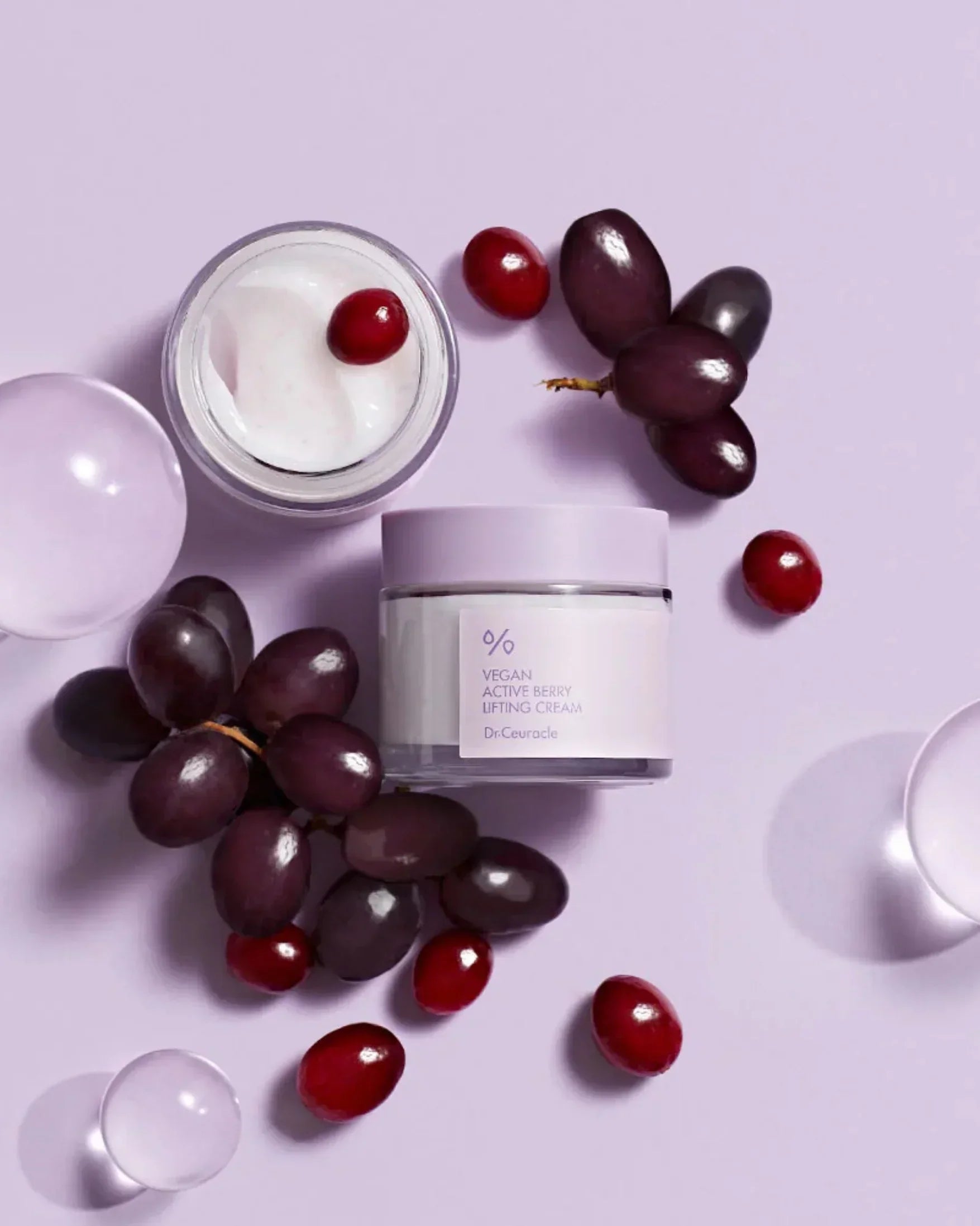 Vegan Active Berry Lifting Cream jar with open lid and cream, surrounded by grapes and red berries on lavender background