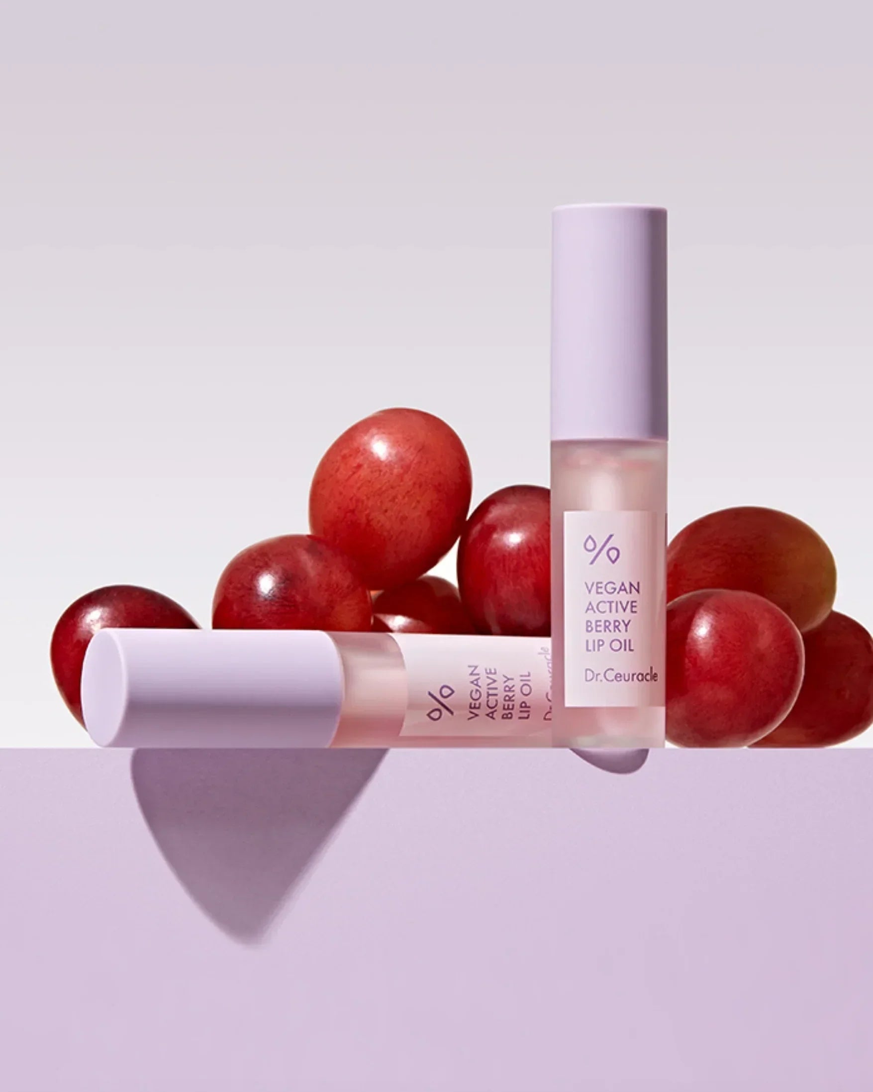 Two Dr.Ceuracle Vegan Active Berry Lip Oil tubes with red berries on a light purple surface