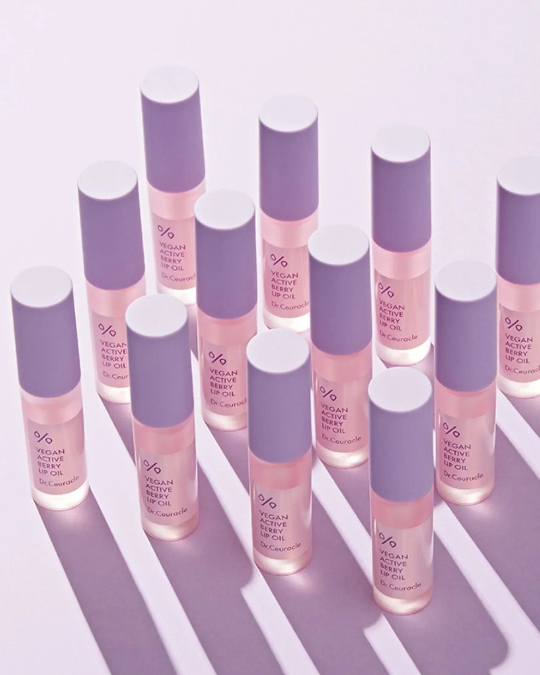 Multiple bottles of Dr. Ceuracle Vegan Active Berry Lip Oil with purple caps on a light background