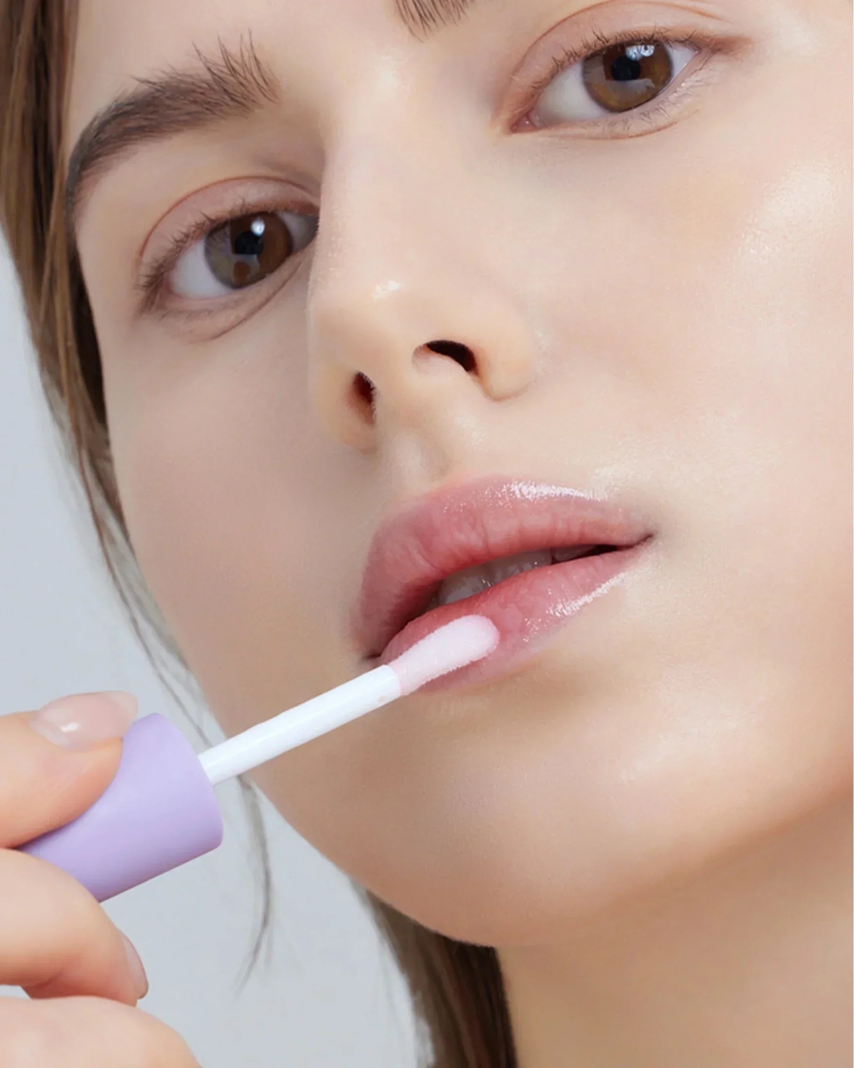 Close-up of woman applying pink vegan berry lip oil with purple applicator wand