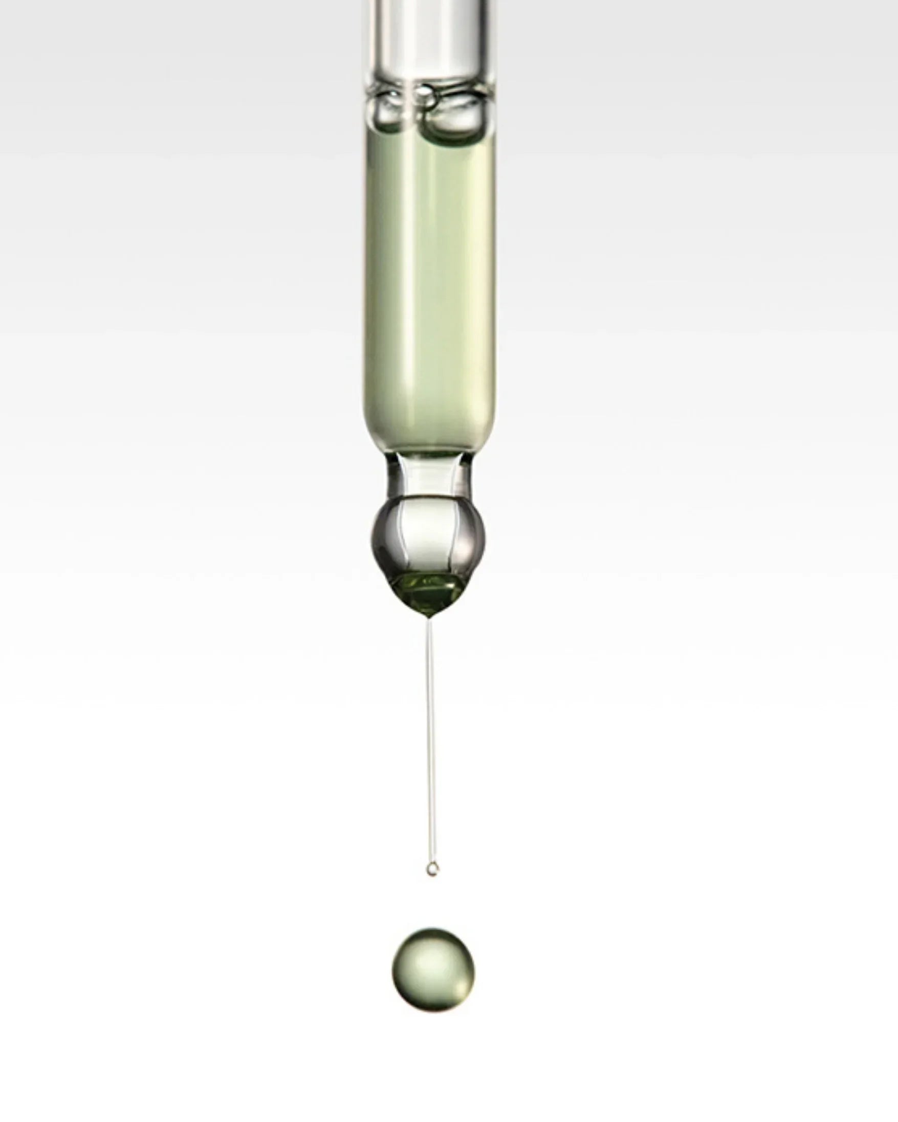 Close-up of green serum drop falling from glass dropper on white background