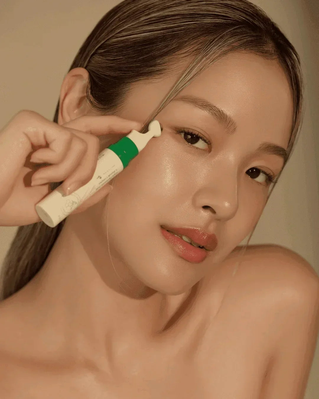 Woman applying vegan collagen eye serum with green and white packaging on glowing skin