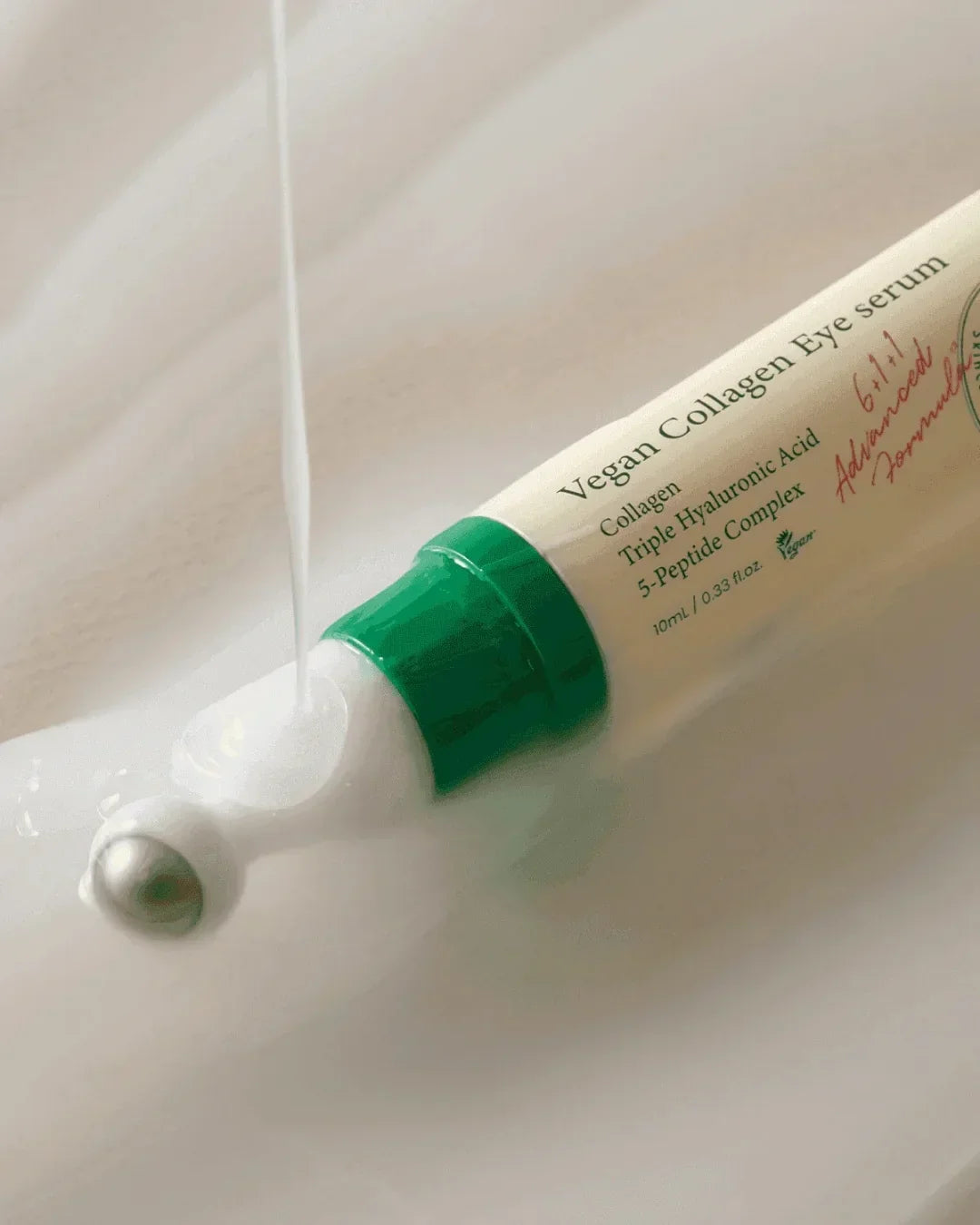 Vegan Collagen Eye Serum tube with green cap and rolling applicator dispensing cream on white surface