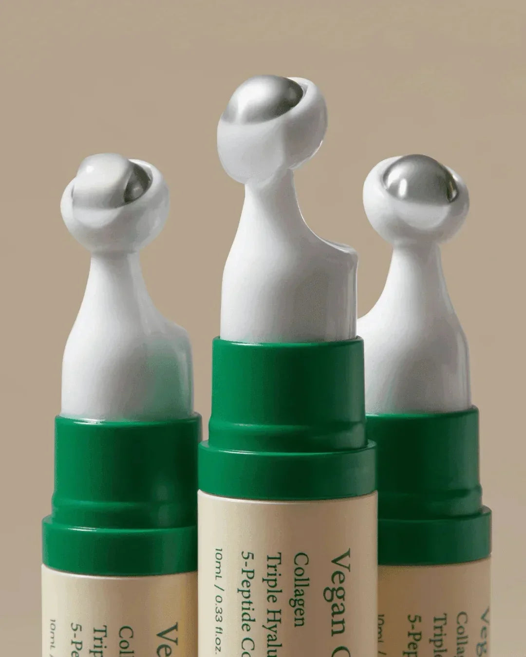 Close-up of vegan collagen eye serum bottles with green caps and rollerball applicators on beige background