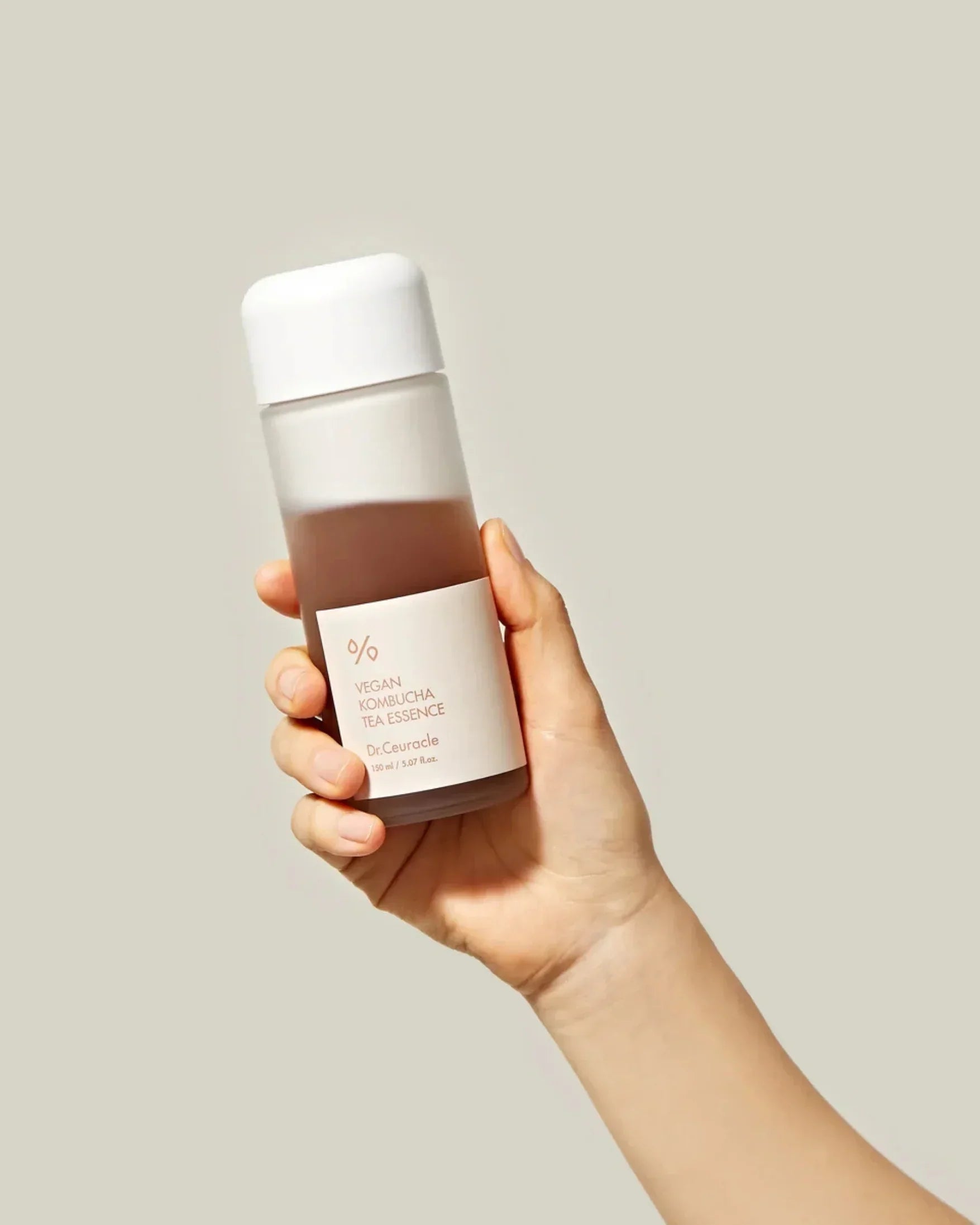 Hand holding Dr.Ceuracle Vegan Kombucha Tea Essence bottle on neutral background
