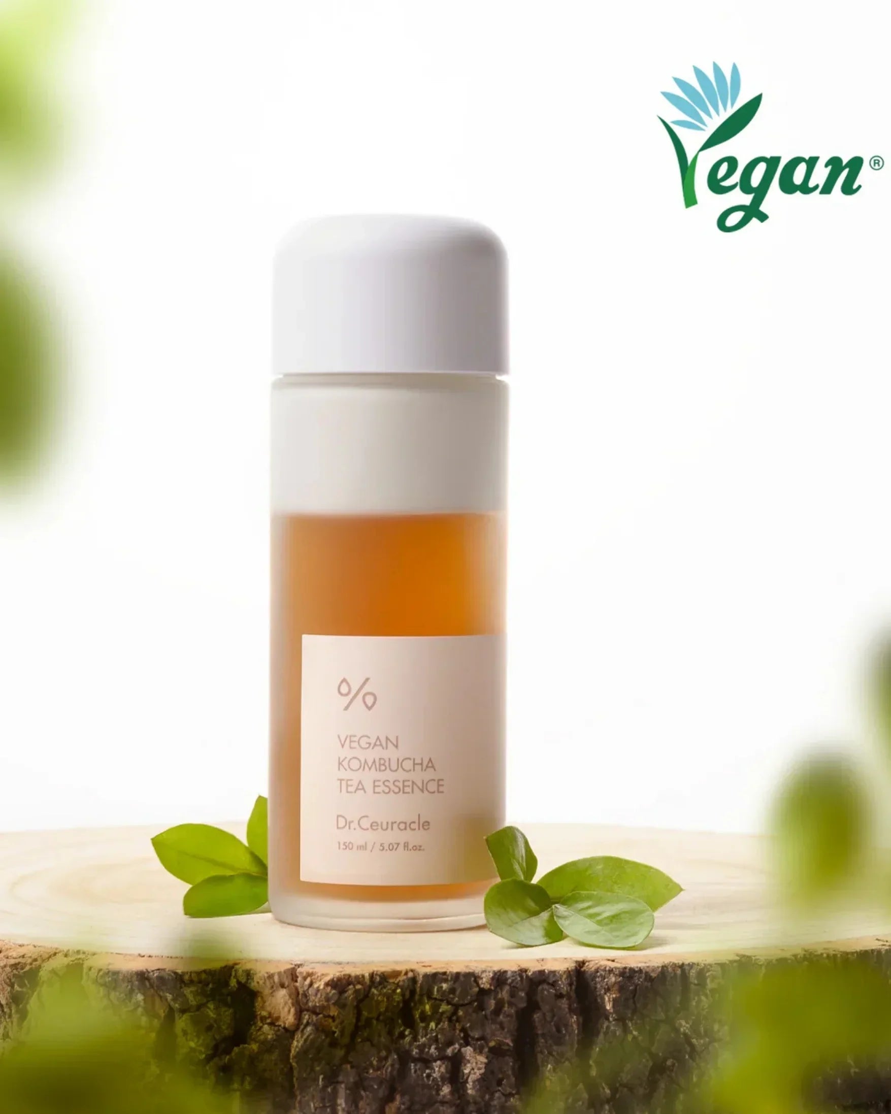 Dr. Ceuracle Vegan Kombucha Tea Essence 150ml bottle on wood slice with green leaves and vegan logo