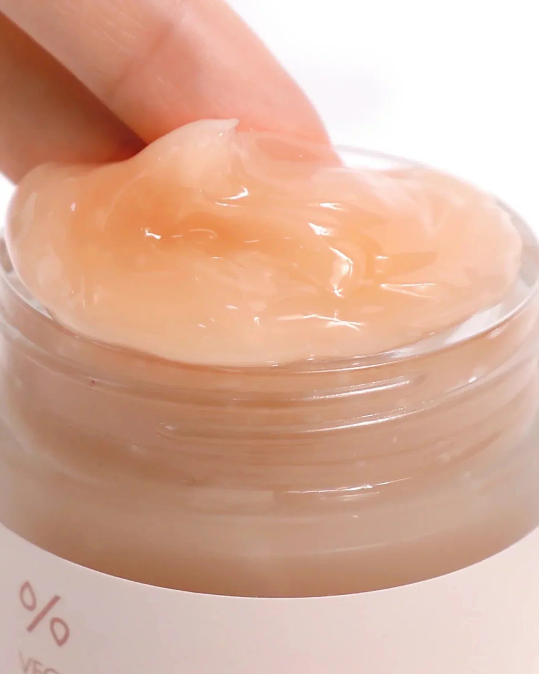 Finger scooping peach-colored vegan kombucha tea gel cream from a clear glass jar