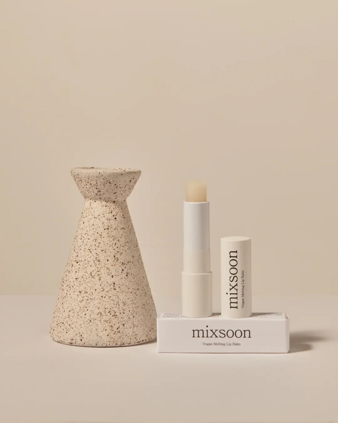 Mixsoon vegan melting lip balm tube and open balm stick on matching box with beige speckled ceramic vase