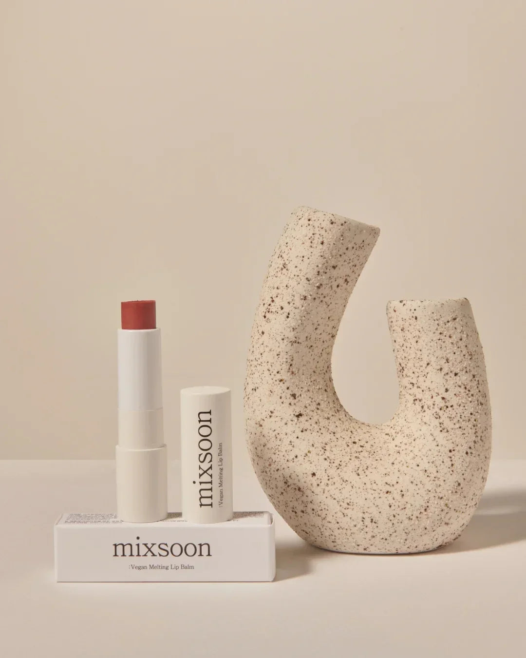 Mixsoon vegan melting lip balm with red tint and minimalist speckled beige sculpture on neutral background
