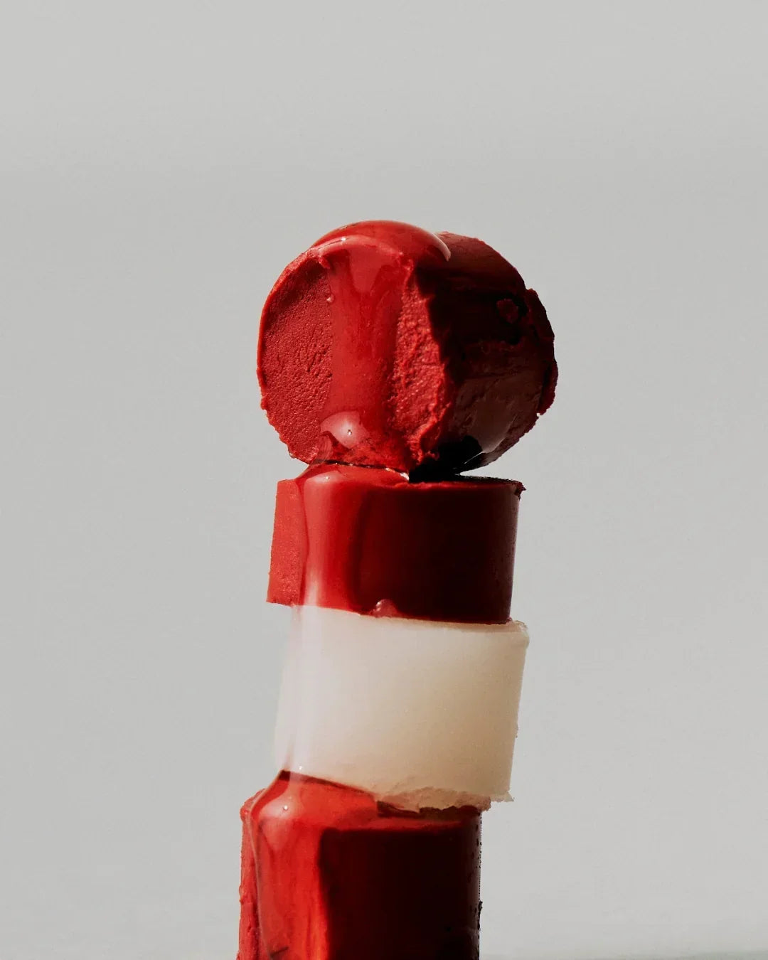 Close-up of melting red vegan lip balm with creamy texture on a plain background