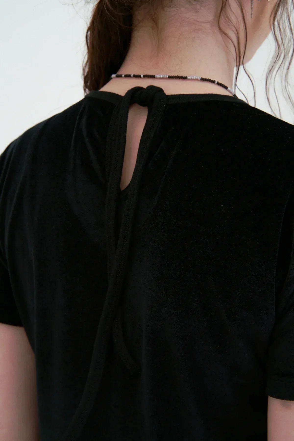 Close-up of a black velvet t-shirt back with a tied keyhole detail and beaded necklace