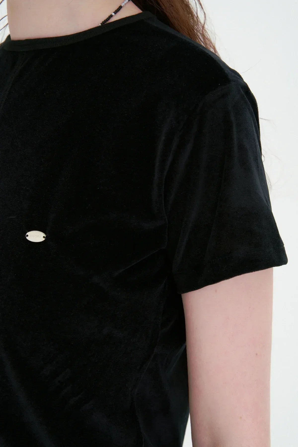 Close-up of black velvet short-sleeve t-shirt worn by person with light skin and necklace