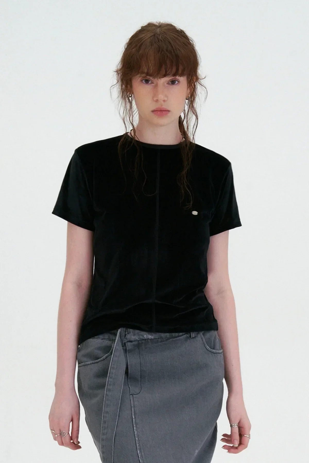 Young woman wearing black velvet short-sleeve t-shirt and gray denim skirt against white background