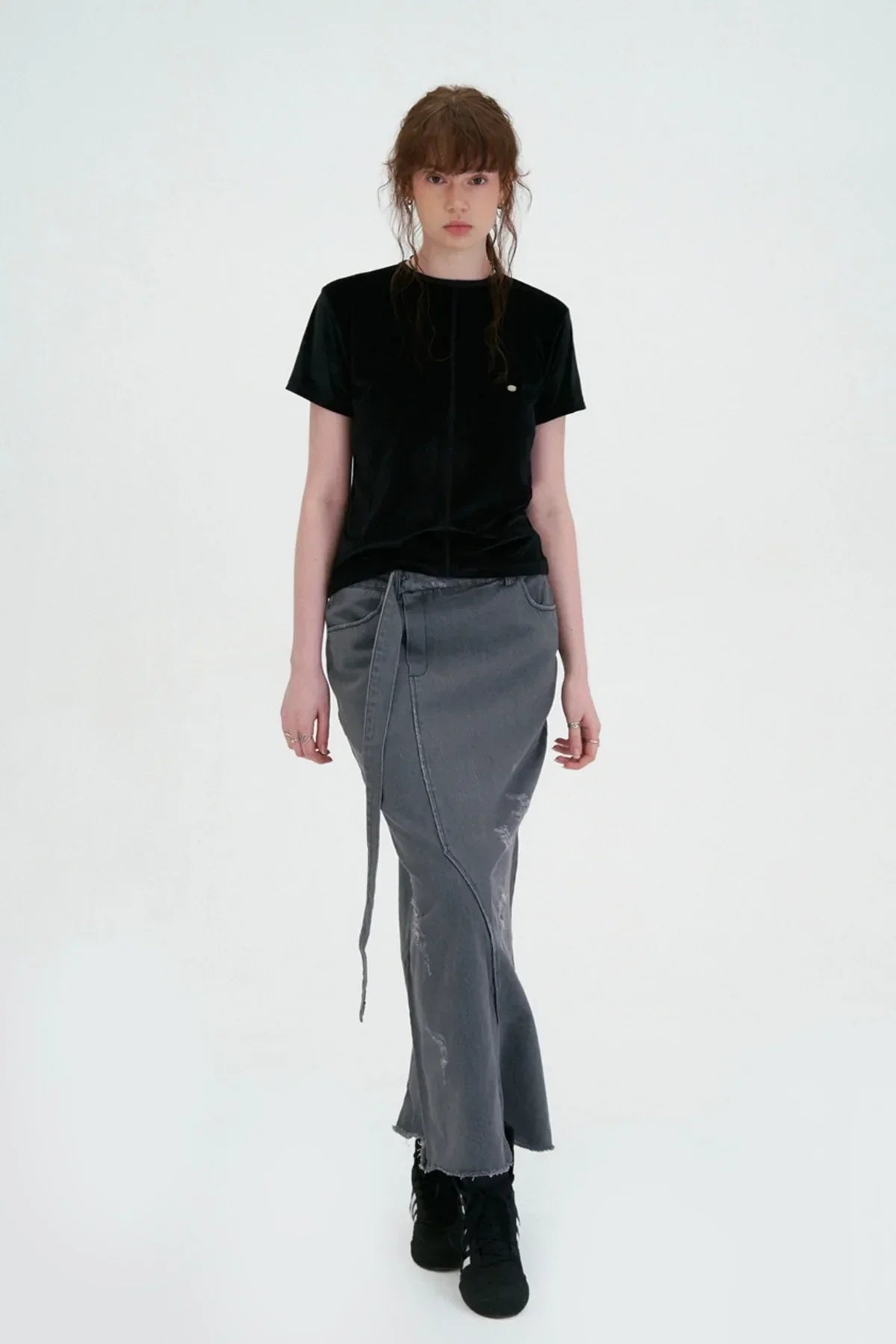 Model wearing black velvet logo t-shirt paired with a gray distressed long skirt and black sneakers