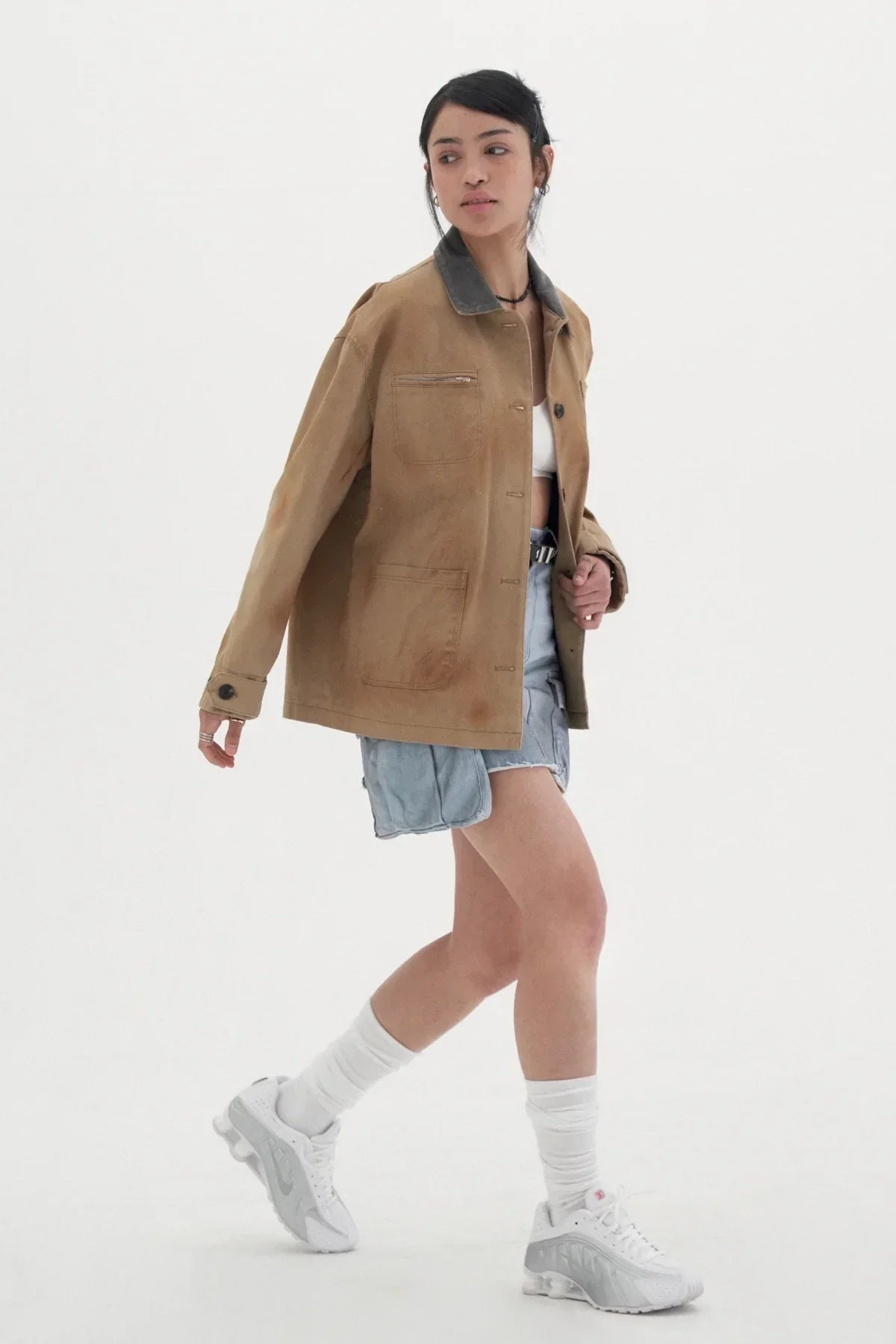 Woman wearing vintage beige work jacket with dark collar, denim shorts, white socks, and sneakers