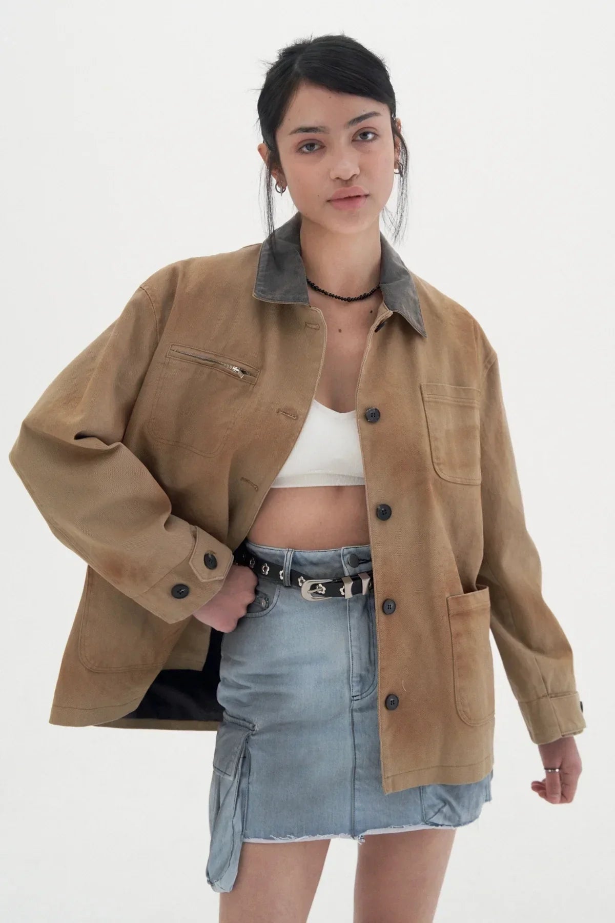 Young woman wearing beige vintage work jacket with dark collar and light denim skirt in studio